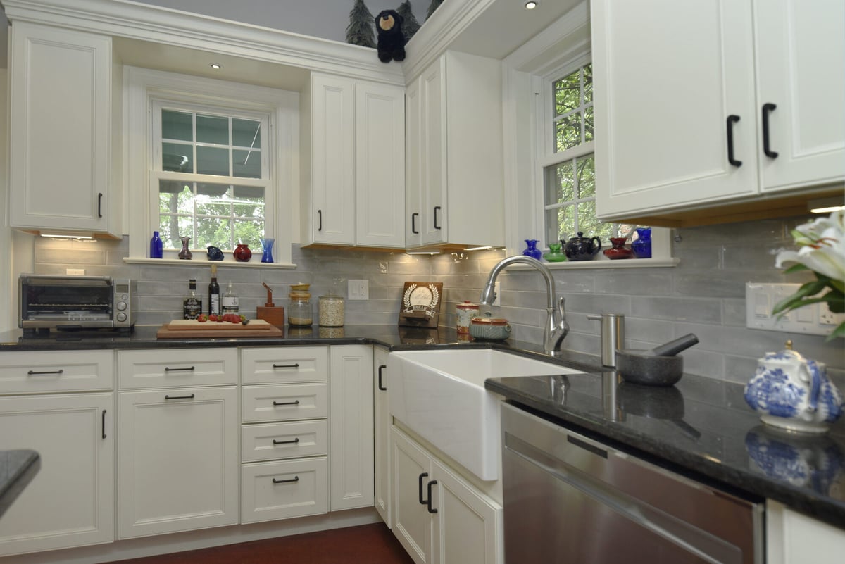 Elegant white kitchen with a farmhouse sink and black countertops in a remodeled Annapolis home by Villa Builders