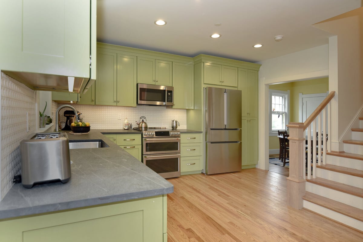 Modern kitchen with green cabinets and stainless steel appliances in a remodeled home by Villa Builders in Annapolis, MD